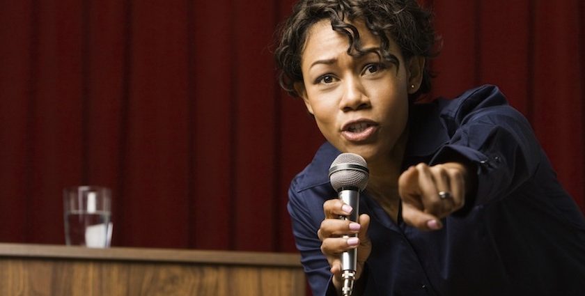 Mixed race businesswoman speaking on stage and pointing